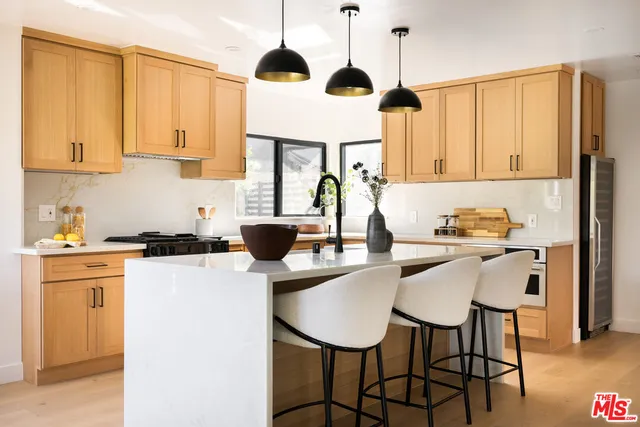 a kitchen with stainless steel appliances granite countertop a stove a refrigerator a sink a dining table and chairs with wooden floor