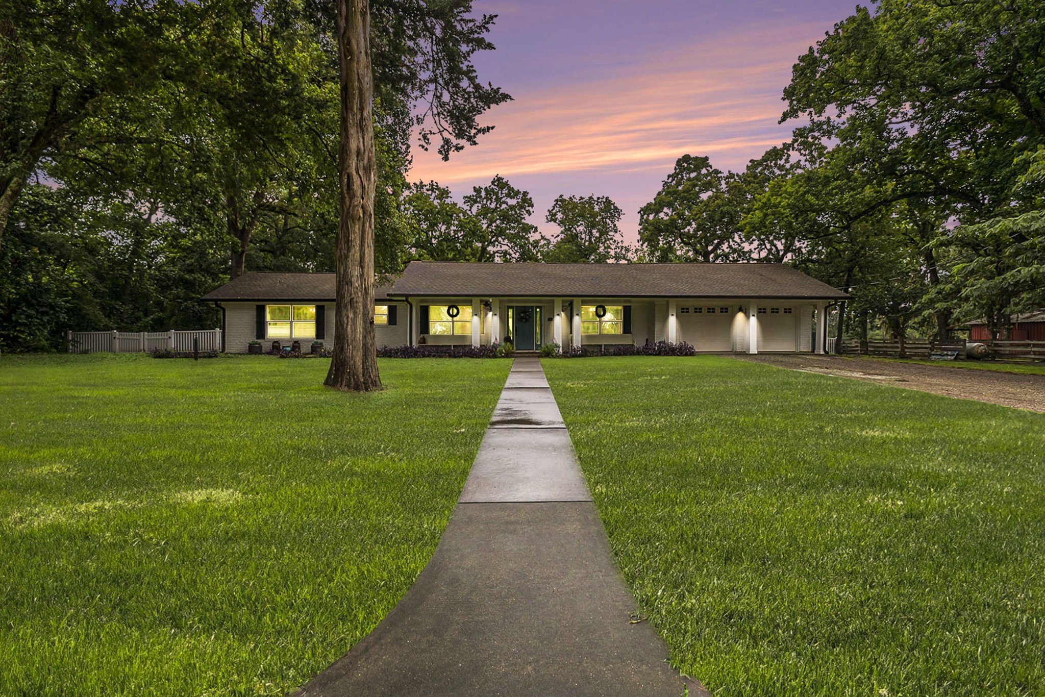 Charming home, beautifully illuminated at twilight, with expansive front yard and inviting pathway.