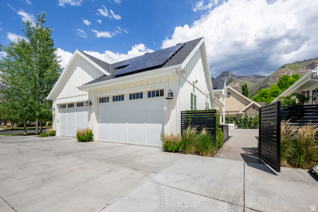 630 East Center Street Alpine, UT 84004 - Photo 82 of 115 Modern farmhouse exterior with white board and batten siding, multiple garage doors with window accents, solar panels, a paved driveway, and black slatted fencing