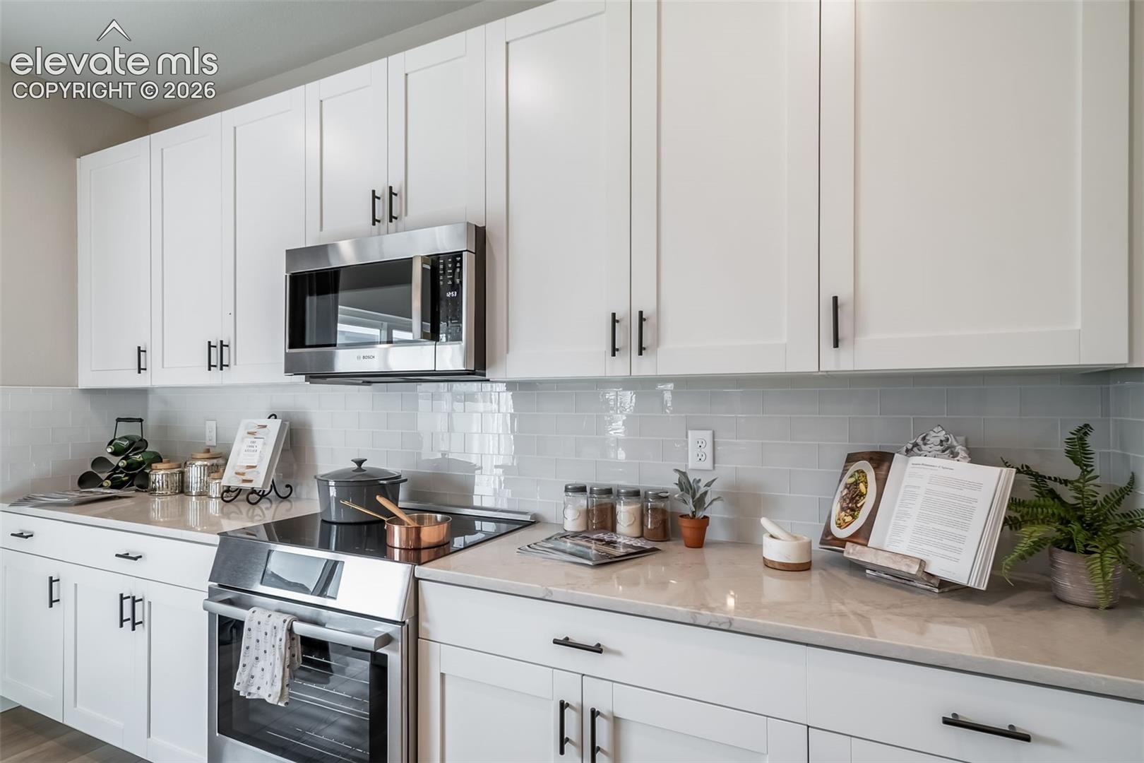 4876 Truscott Road Colorado Springs, CO 80925 - Photo 19 of 28 Kitchen featuring extensive white shaker cabinetry, stainless steel appliances, light-toned countertops, and a subway tile backsplash
*Photos of a model home*