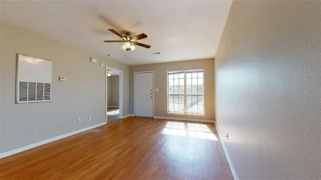 a view of an empty room with wooden floor and a window