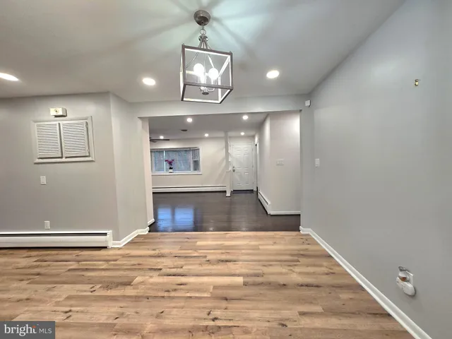 a view of an empty room and kitchen with wooden floor