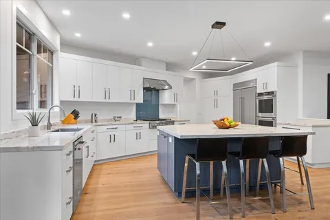 a kitchen with stainless steel appliances granite countertop a stove top oven a sink dishwasher and white cabinets with wooden floor