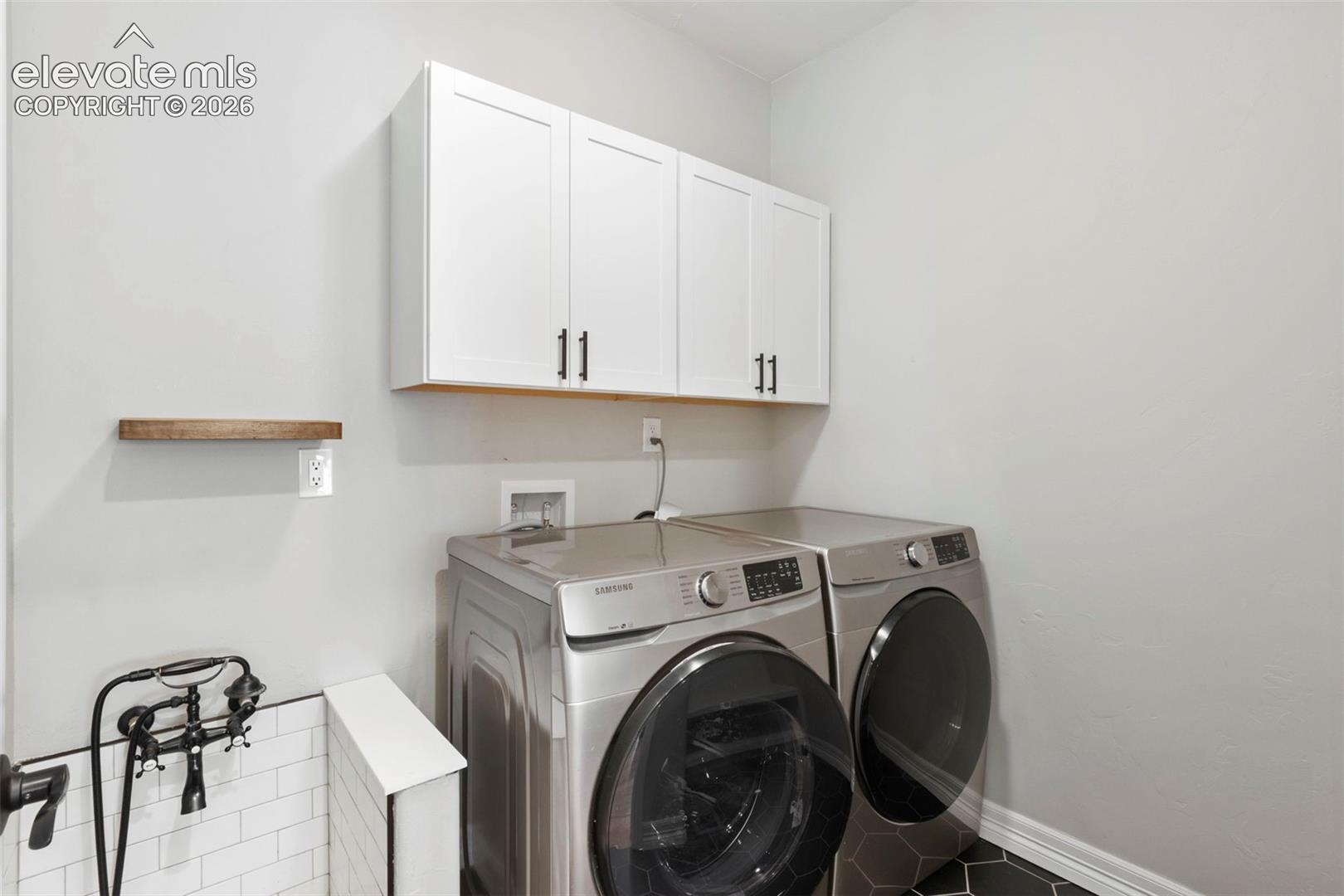 5375 Old Star Ranch View Colorado Springs, CO 80906 - Photo 18 of 47 Laundry area featuring front-load washer and dryer, white cabinetry with dark hardware, a wood-finish floating shelf, and a pet washing station with subway tile surround and black hexagonal floor tile