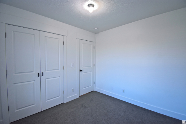 2480 West 450 South, Unit 2 Springville, UT 84663 - Photo 14 of 19 Unfurnished bedroom with dark carpet, a closet, and a textured ceiling