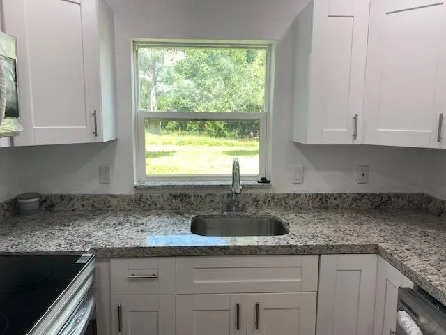 a kitchen with granite countertop a sink window and cabinets