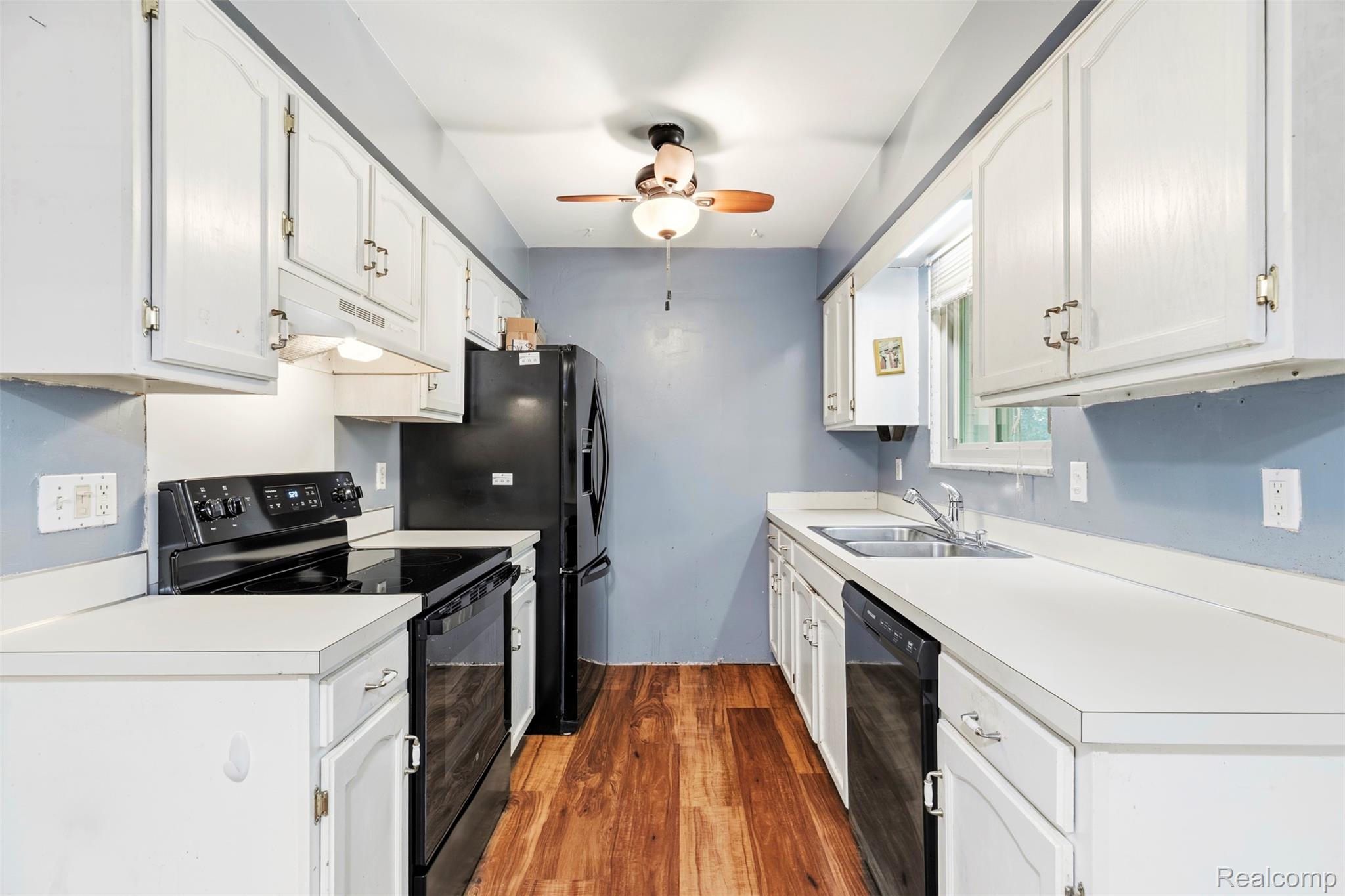 309 Windy Bluff Street Flushing, MI 48433 - Photo 3 of 32 Kitchen featuring abundant white cabinetry, light countertops, wood-finish flooring, a full suite of black appliances, and a double basin sink