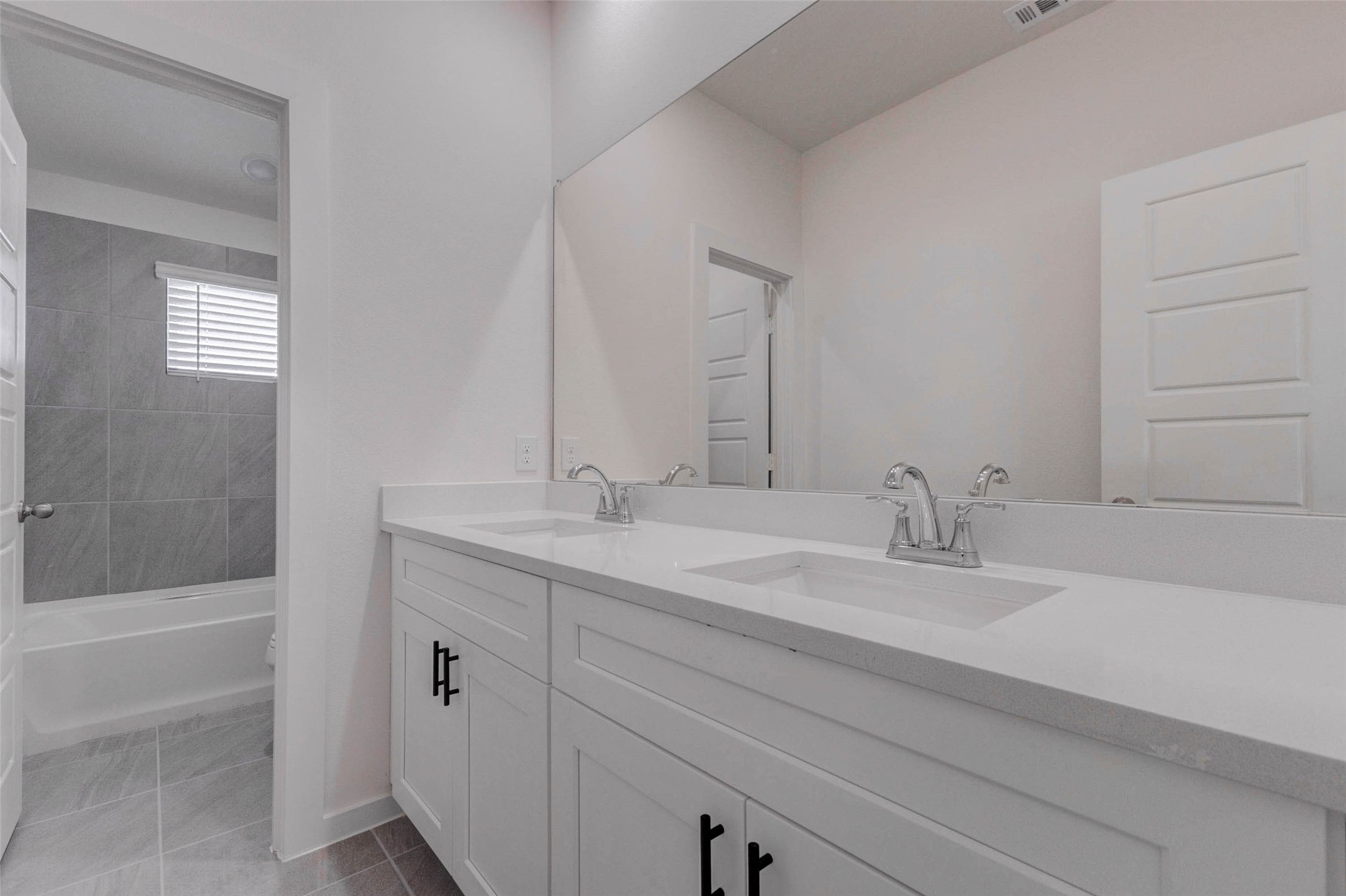 1206 Hemet Court Rosharon, TX 77583 - Photo 17 of 21 Secondary bathroom with a long double-sink vanity, large mirror, white cabinetry, black hardware, gray tile flooring, and a separate tub/shower area. The dual sinks add everyday convenience, while the neutral finishes and clean design create a fresh, functional space for bedrooms, guests, or shared use.