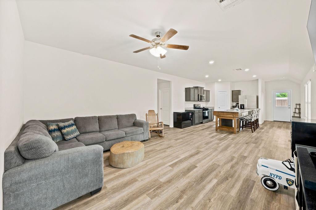 822 Ramble Road Lavon, TX 75166 - Photo 16 of 35 Open-concept living area featuring wood-finish flooring throughout, a vaulted ceiling with a ceiling fan, recessed lighting, and a kitchen with dark cabinetry and a central island