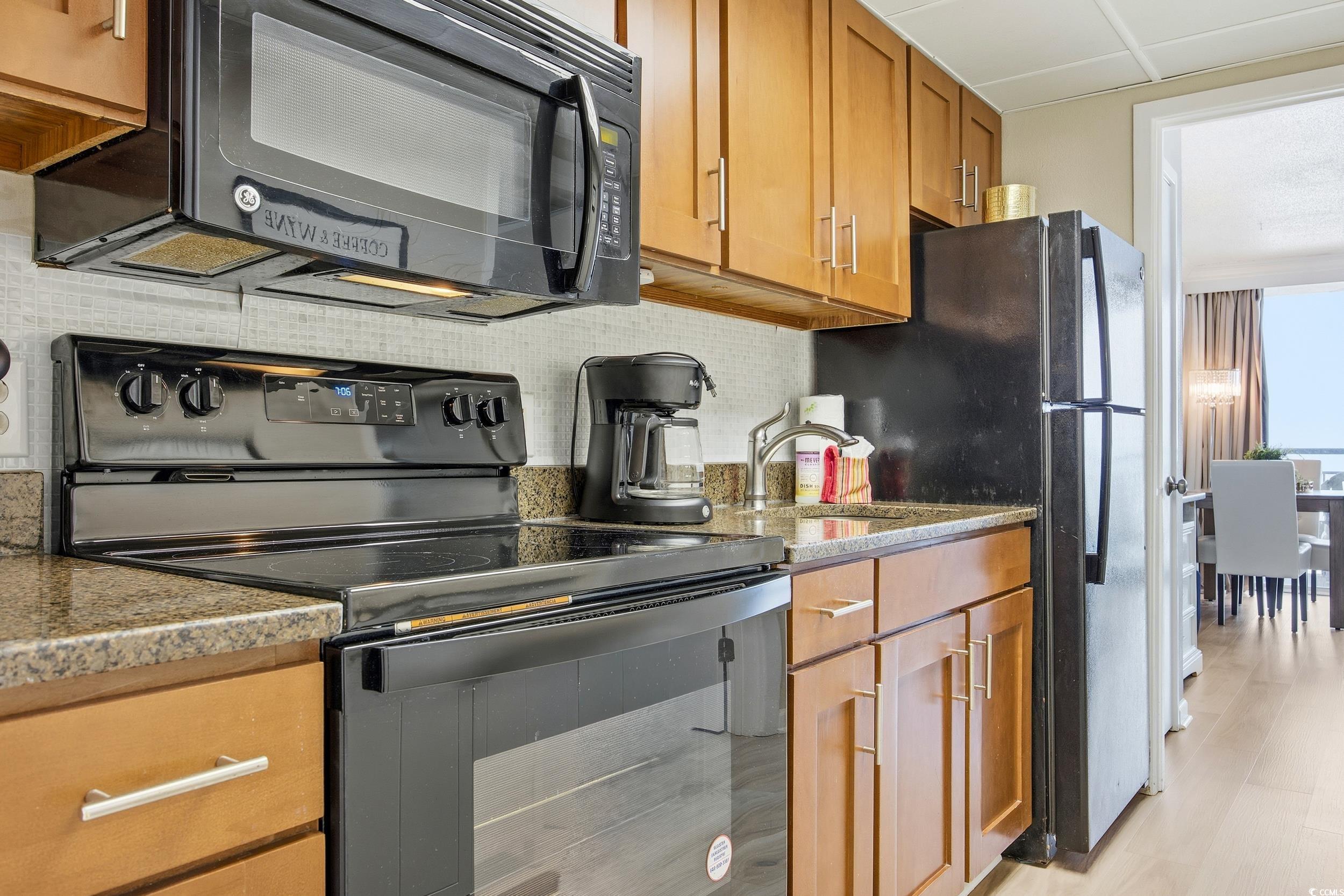 1105 South Ocean Boulevard, Unit 932 Myrtle Beach, SC 29577 - Photo 14 of 32 Kitchen featuring black appliances, brown cabinets, backsplash, and light stone countertops