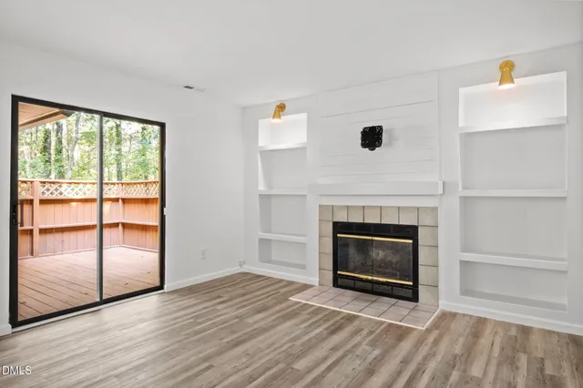 an empty room with wooden floor fireplace and windows