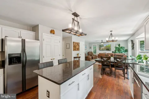 a kitchen with stainless steel appliances granite countertop a kitchen island a stove a refrigerator a dining table chairs and couches with wooden floor