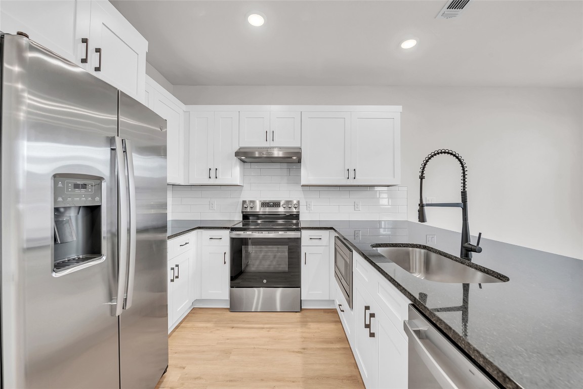 7600 Strong Bow Court Austin, TX 78744 - Photo 8 of 26 Kitchen featuring stainless steel appliances, dark stone countertops, tasteful backsplash, white cabinets, and recessed lighting