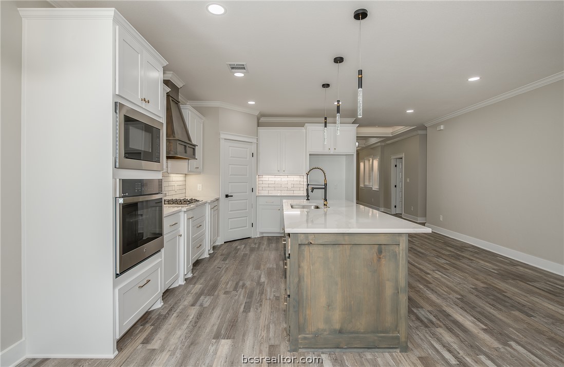 2908 GOLDBERG Drive Bryan, TX 77808 - Photo 20 of 44 Modern kitchen features: stainless steel appliances, quartz countertops, stained island, painted cabinets, decorative pendant lights, cabinet hardware, vinyl flooring, and tile backsplash.