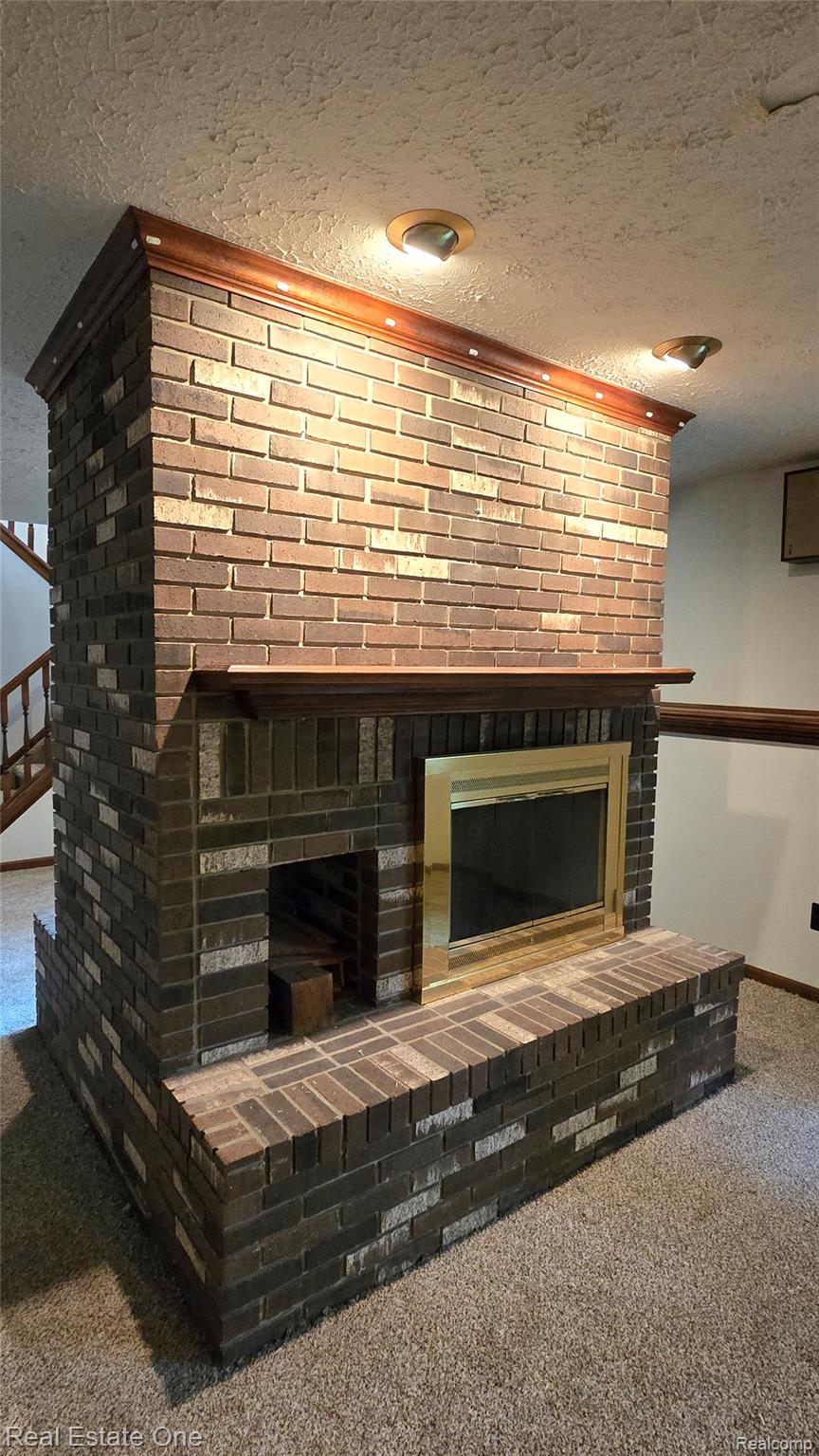 8950 Wise Road Commerce Township, MI 48382 - Photo 29 of 39 Brick fireplace featuring a brass-framed firebox, built-in log storage, and a substantial brick hearth
