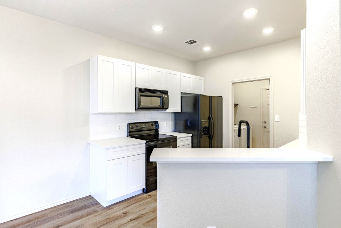 2632 Century Park Boulevard, Unit 18 Austin, TX 78727 - Photo 3 of 32 Kitchen featuring black appliances, white cabinets, light wood-type flooring, tasteful backsplash, and a peninsula
