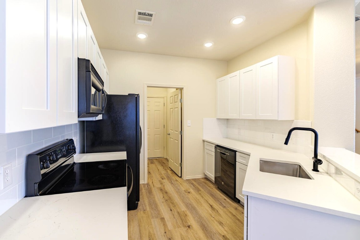 2632 Century Park Boulevard, Unit 18 Austin, TX 78727 - Photo 5 of 32 Kitchen featuring backsplash, white cabinetry, light stone countertops, light wood-style flooring, and black appliances
