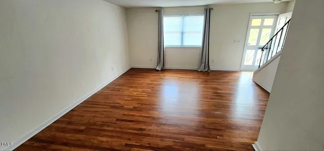 an empty room with wooden floor and windows with curtains