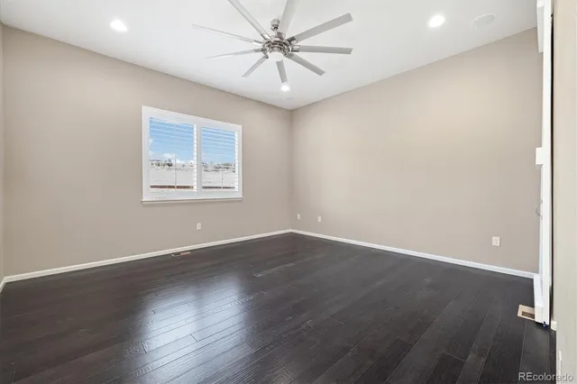 an empty room with wooden floor chandelier fan and windows