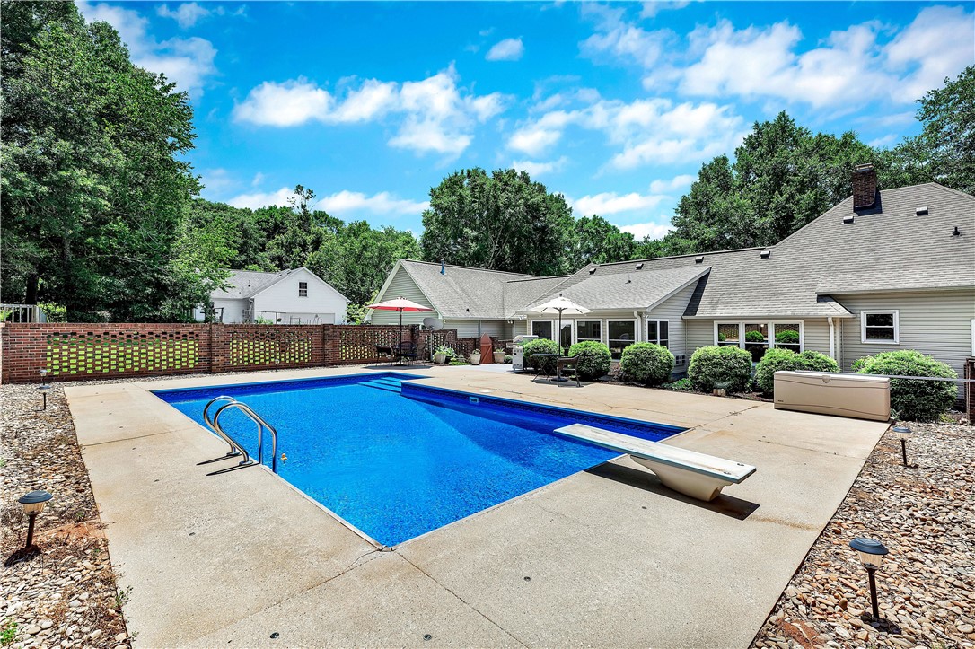 910 Chantilly Lane Anderson, SC 29625 - Photo 33 of 38 A private backyard oasis features a glistening pool with a diving board, framed by a charming brick fence and lush greenery.