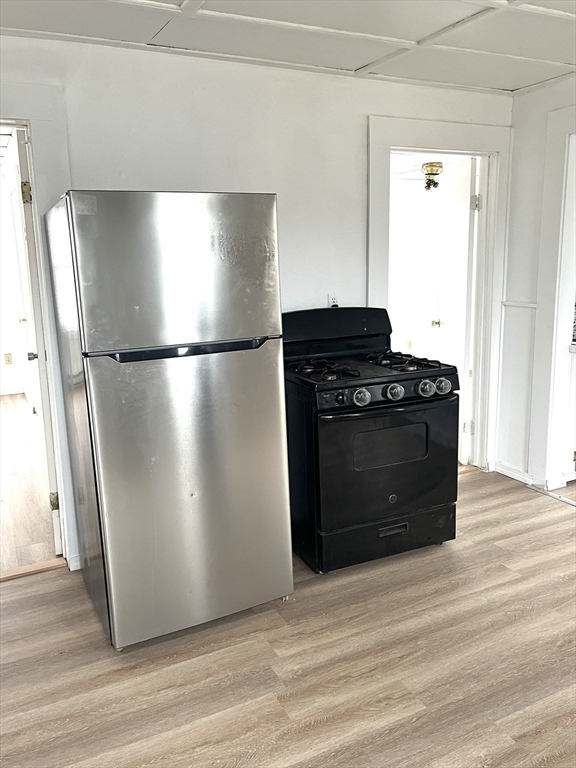 92 Emory Street, Unit 1 Attleboro, MA 02703 - Photo 2 of 8 a view of a refrigerator in kitchen and an empty room with wooden floor