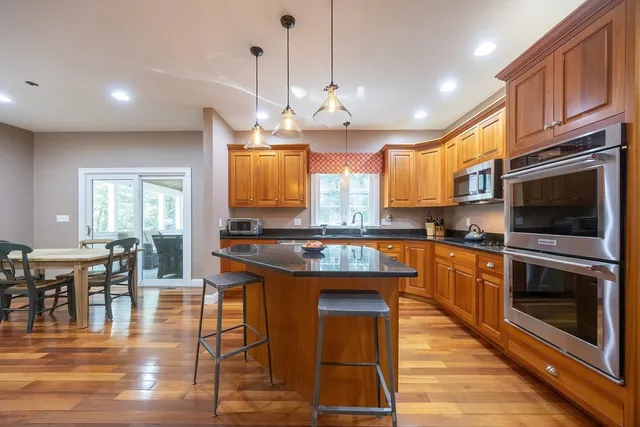 a kitchen with stainless steel appliances granite countertop a stove top oven a sink a dining table and chairs with wooden floor