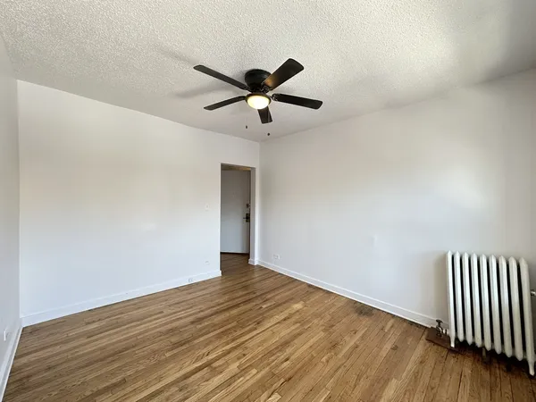 a view of an empty room with wooden floor and a ceiling fan