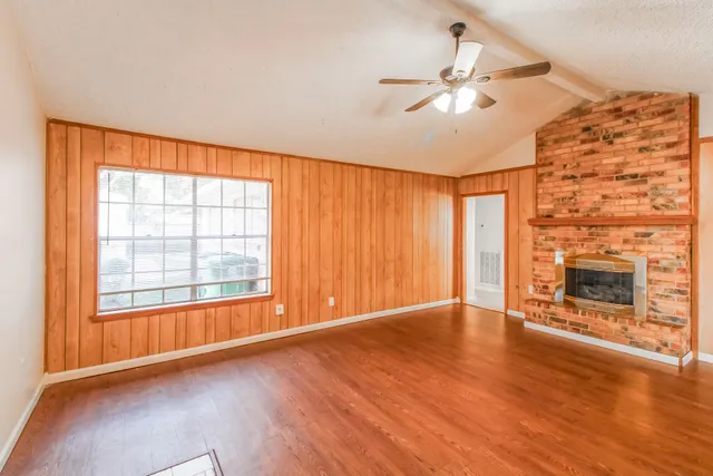 an empty room with wooden floor fireplace and windows