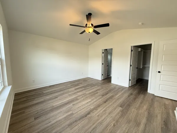 an empty room with wooden floor a ceiling fan and kitchen view