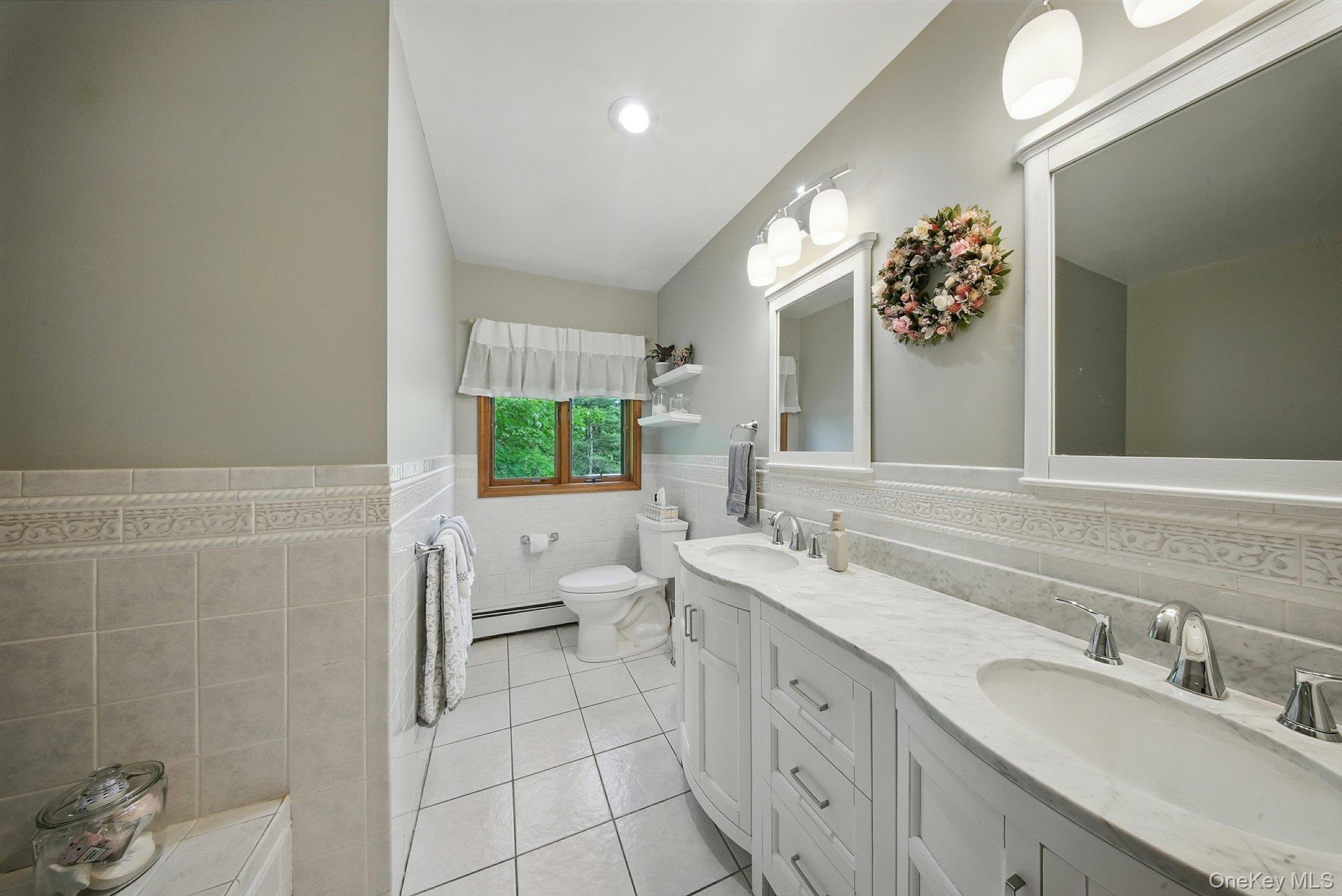 193 Dill Road Forestburgh, NY 12777 - Photo 16 of 31 Bathroom featuring a baseboard heating unit, tile walls, double vanity, tile patterned floors, and a wainscoted wall