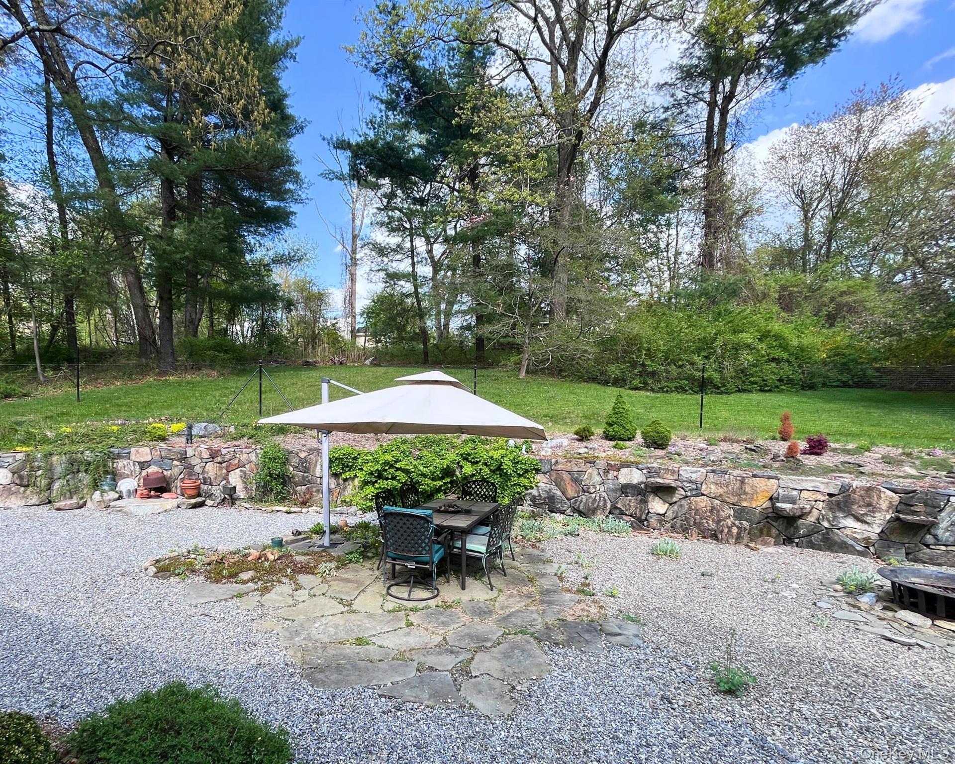 64 Belden Road Carmel, NY 10512 - Photo 17 of 23 Patio with table, umbrella, and fire pit surrounded by lush landscaping