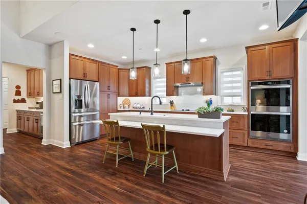 a kitchen with stainless steel appliances granite countertop a refrigerator a oven a sink a dining table and chairs with wooden floor