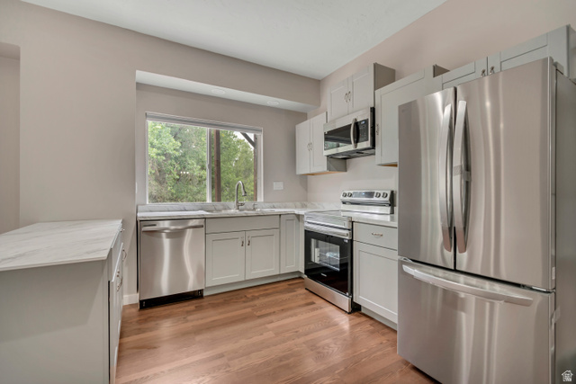 2154 Wasatch Boulevard Sandy, UT 84092 - Photo 46 of 55 Kitchen with appliances with stainless steel finishes, light wood-style flooring, light stone countertops, white cabinets, and a peninsula
