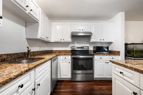 a kitchen with kitchen island granite countertop stainless steel appliances a stove a sink and white cabinets