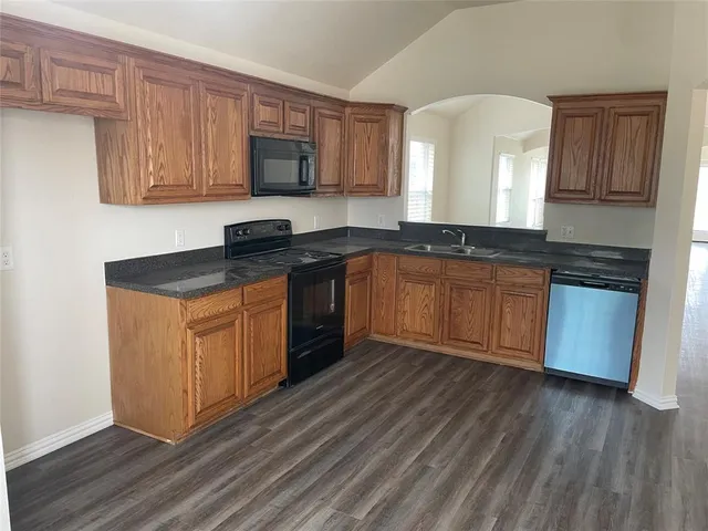 a kitchen with stainless steel appliances granite countertop wooden cabinets a stove a sink and a hard wood floors