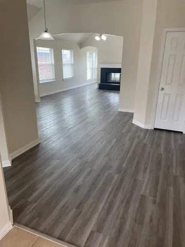 a view of empty room with wooden floor and kitchen