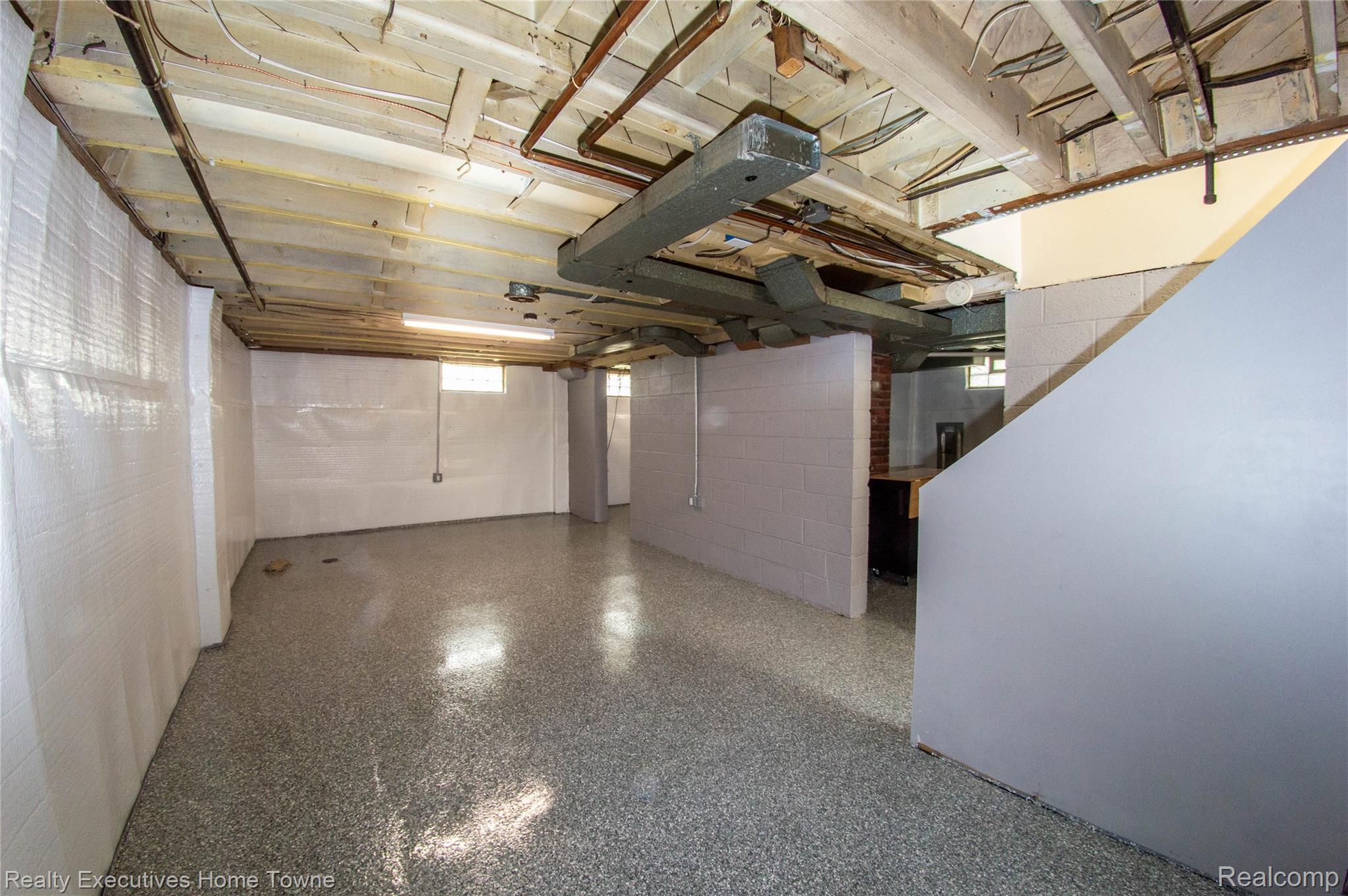 2676 Cumberland Road Berkley, MI 48072 - Photo 28 of 38 Expansive basement area featuring exposed ceiling joists, concrete block walls, and a durable speckled epoxy floor finish