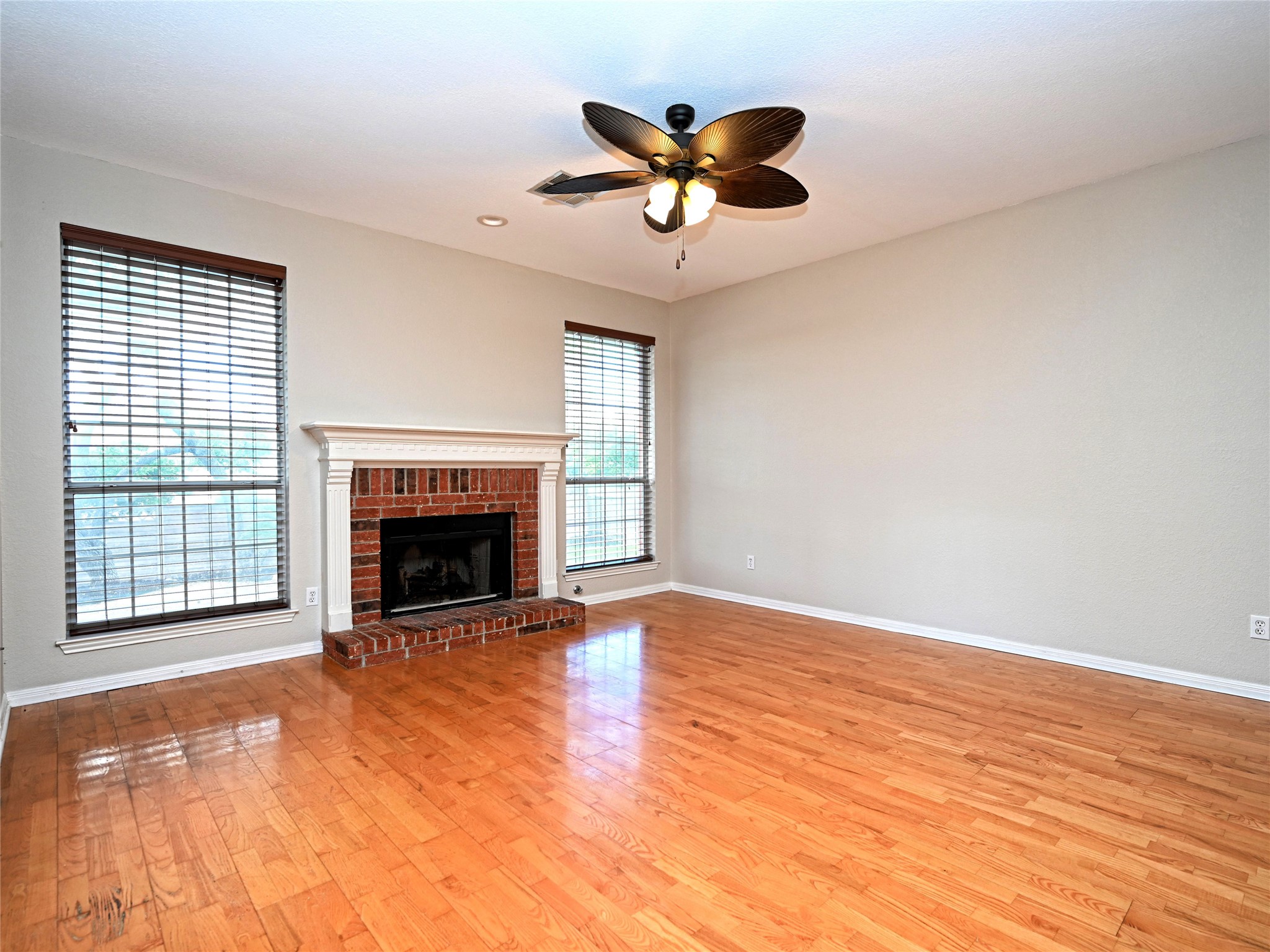 11017 Rio Vista Drive Austin, TX 78726 - Photo 12 of 38 Living area featuring wood-finish flooring, a brick fireplace with a white mantel, and two windows with blinds
