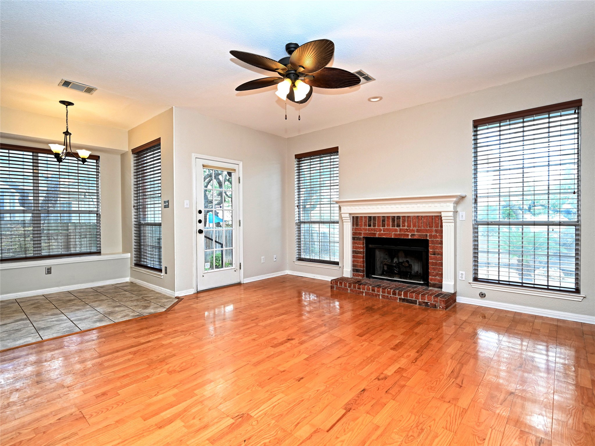 11017 Rio Vista Drive Austin, TX 78726 - Photo 14 of 38 Spacious interior featuring wood-finish flooring, a brick fireplace with a white mantel, and multiple large windows with blinds