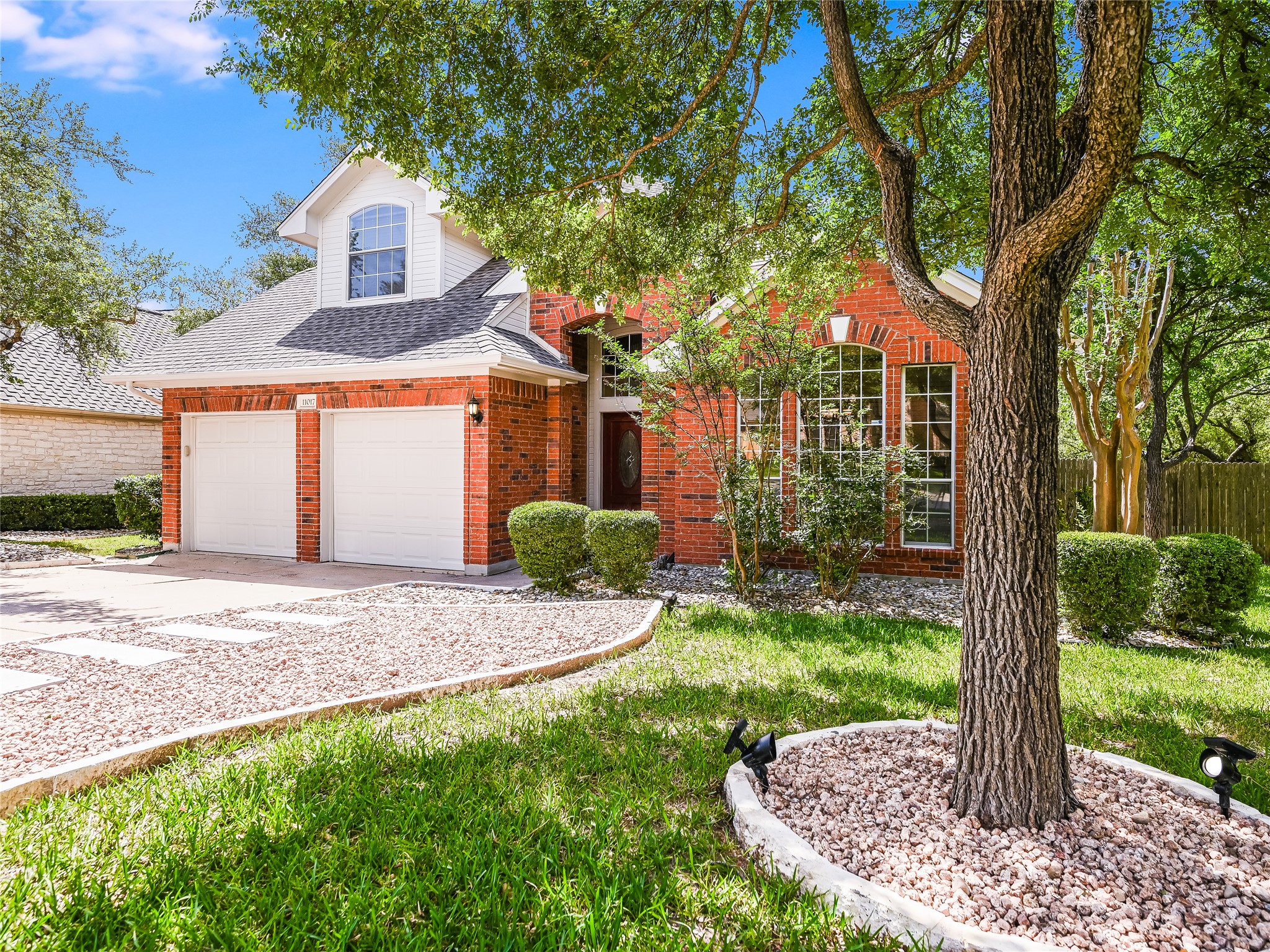 11017 Rio Vista Drive Austin, TX 78726 - Photo 2 of 38 Brick facade residence featuring a two-car garage, an arched dormer window, and mature trees