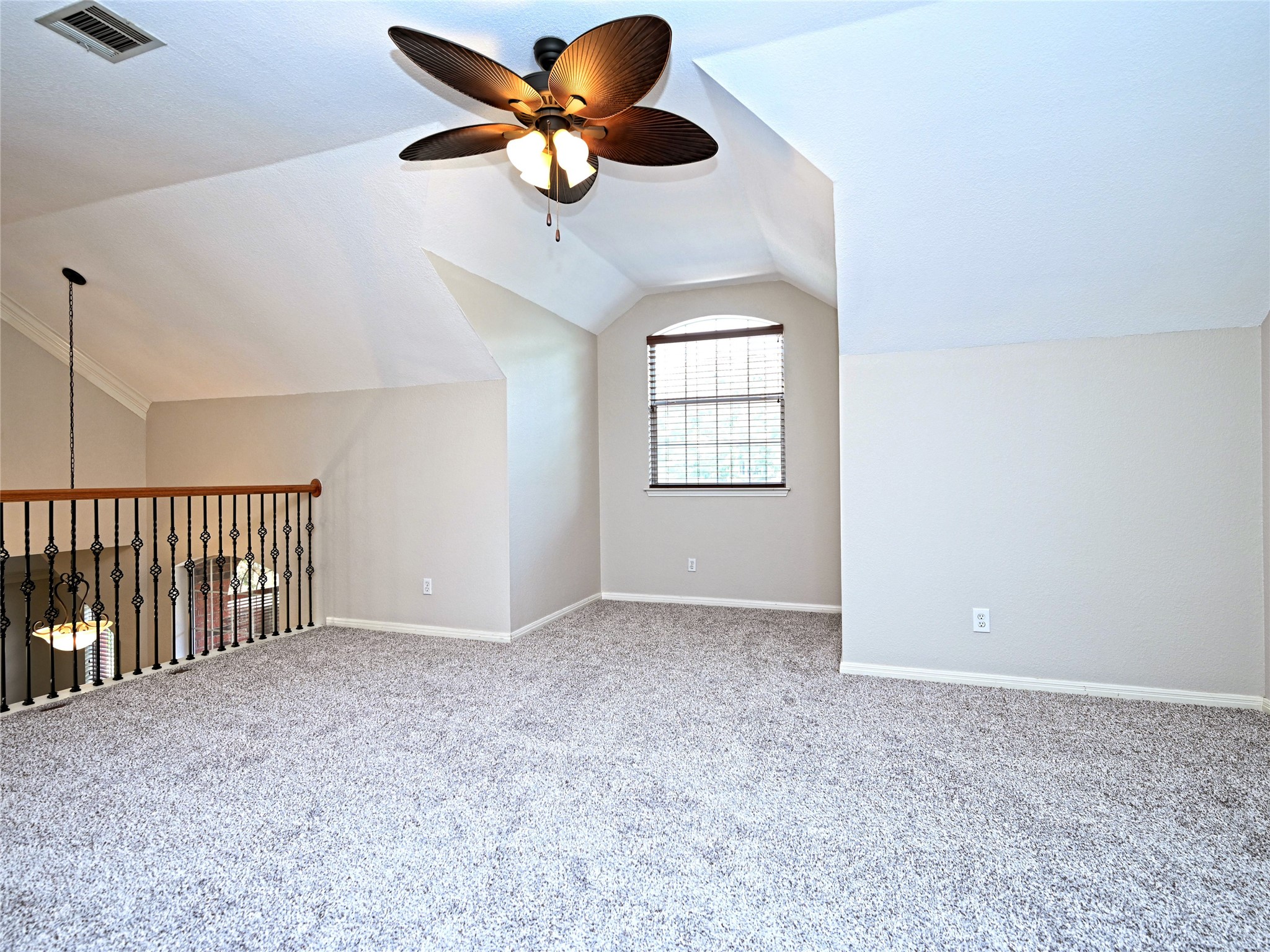 11017 Rio Vista Drive Austin, TX 78726 - Photo 22 of 38 Carpeted loft area featuring a vaulted ceiling with a ceiling fan, a rounded top window with blinds, and a wood and wrought iron railing overlooking a lower space with a chandelier
