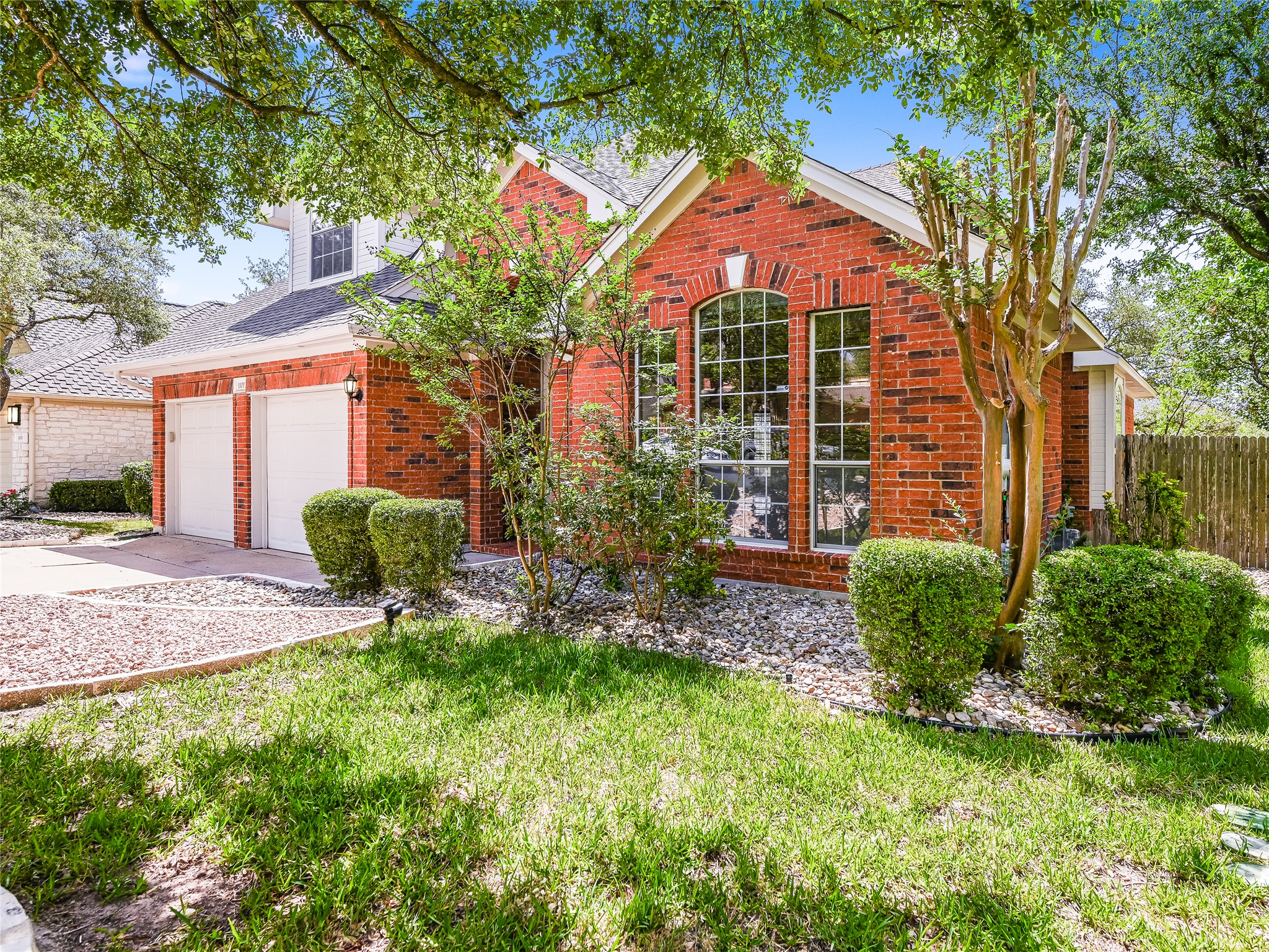 11017 Rio Vista Drive Austin, TX 78726 - Photo 3 of 38 Brick exterior featuring an arched window with mullions, a two-car garage, and mature trees