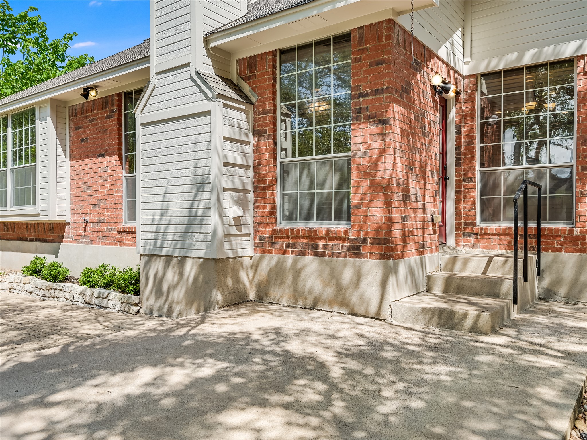 11017 Rio Vista Drive Austin, TX 78726 - Photo 33 of 38 Brick and siding exterior featuring multiple large windows with muntins, a prominent chimney with horizontal siding, and concrete steps with a black metal handrail leading to an entryway