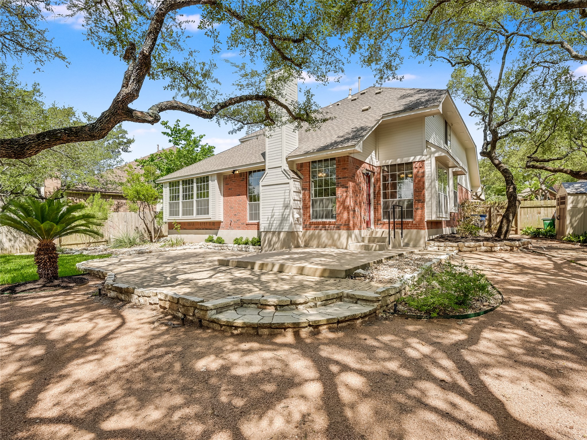 11017 Rio Vista Drive Austin, TX 78726 - Photo 34 of 38 Outdoor patio area featuring a multi-level stone hardscape, mature trees providing natural shade, and a red brick exterior