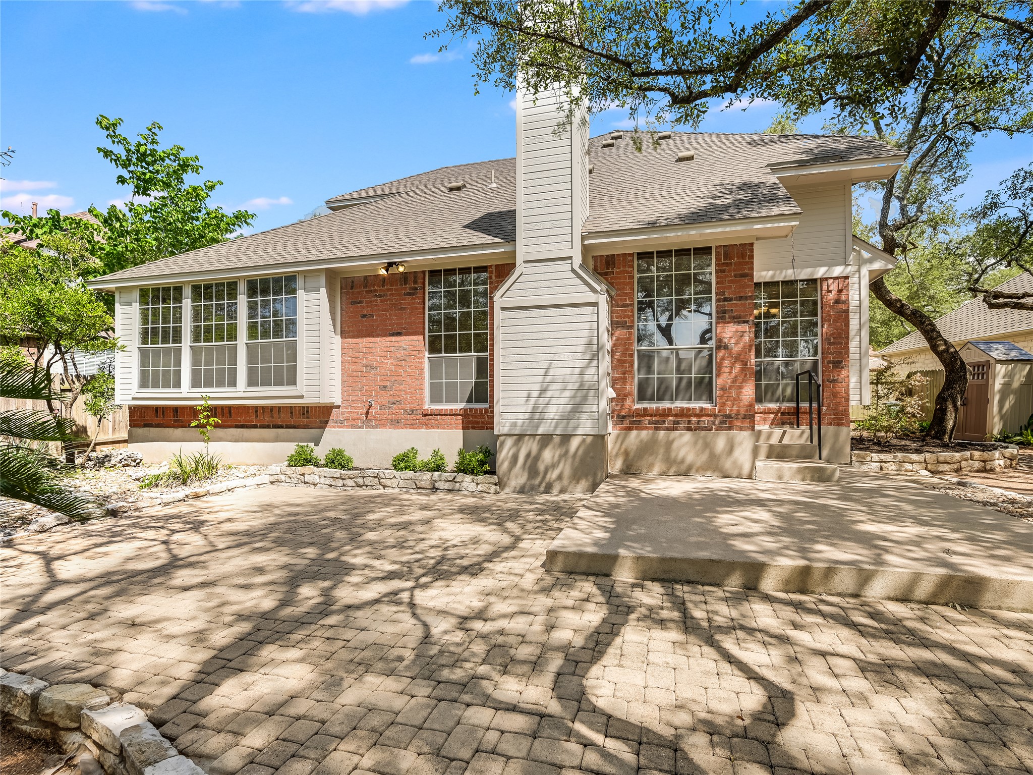 11017 Rio Vista Drive Austin, TX 78726 - Photo 35 of 38 Rear exterior featuring brick and siding construction, multiple windows, a paver patio, a concrete patio, and a stone retaining wall