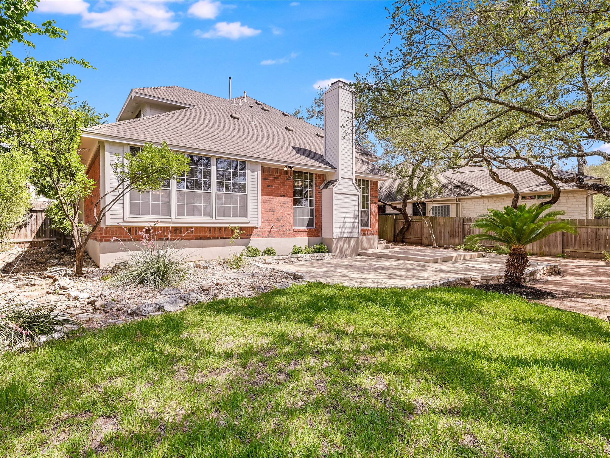 11017 Rio Vista Drive Austin, TX 78726 - Photo 36 of 38 Expansive backyard featuring a manicured lawn, a stone patio, mature trees, and a brick exterior with white trim