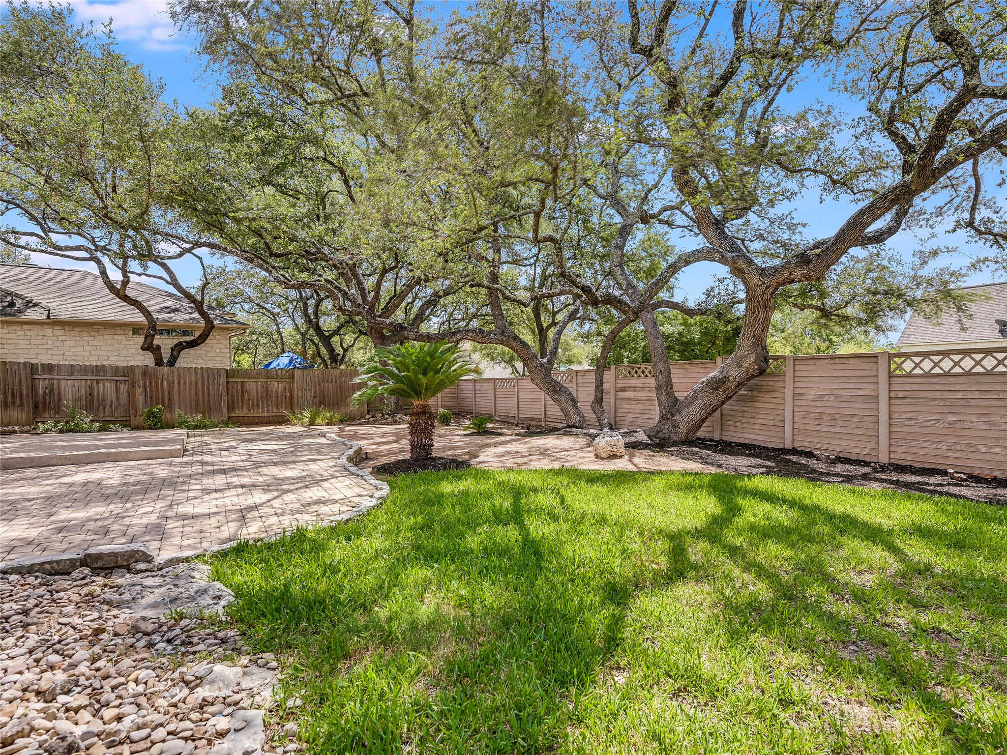 11017 Rio Vista Drive Austin, TX 78726 - Photo 38 of 38 Expansive backyard featuring mature trees, a manicured lawn, a paved patio area, and a decorative privacy fence