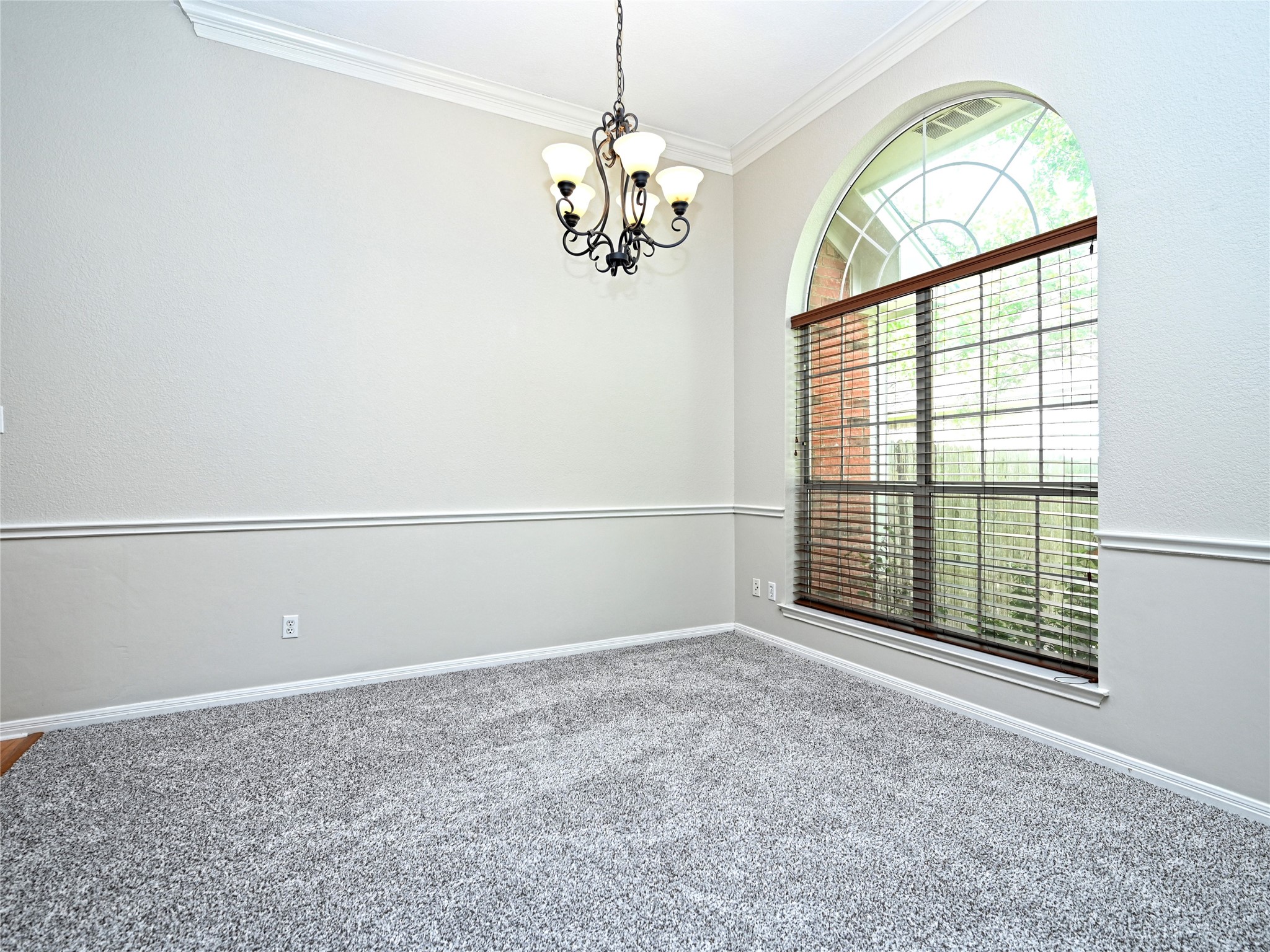 11017 Rio Vista Drive Austin, TX 78726 - Photo 10 of 38 Room featuring a large arched window with blinds, crown molding, chair rail molding, a decorative chandelier, and light gray carpet flooring