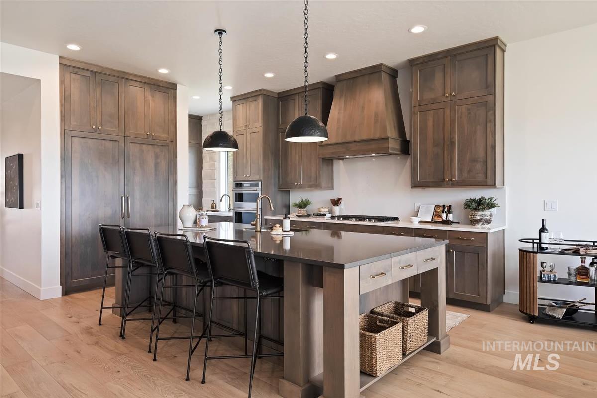 7615 Brown Way Eagle, ID 83714 - Photo 12 of 43 Gourmet kitchen featuring a large central island with seating, extensive wood cabinetry, wood-finish flooring, recessed lighting, and modern pendant fixtures