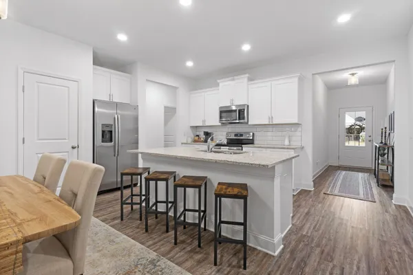 a kitchen with stainless steel appliances granite countertop a table chairs refrigerator a sink a stove a microwave and dining table with wooden floor